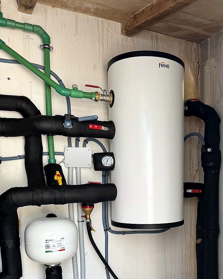 Depósito de agua caliente Ferroli con vaso de expansión, manómetro y tuberías aisladas en el cuarto técnico de una aerotermia en Mallorca, instalación de JSL