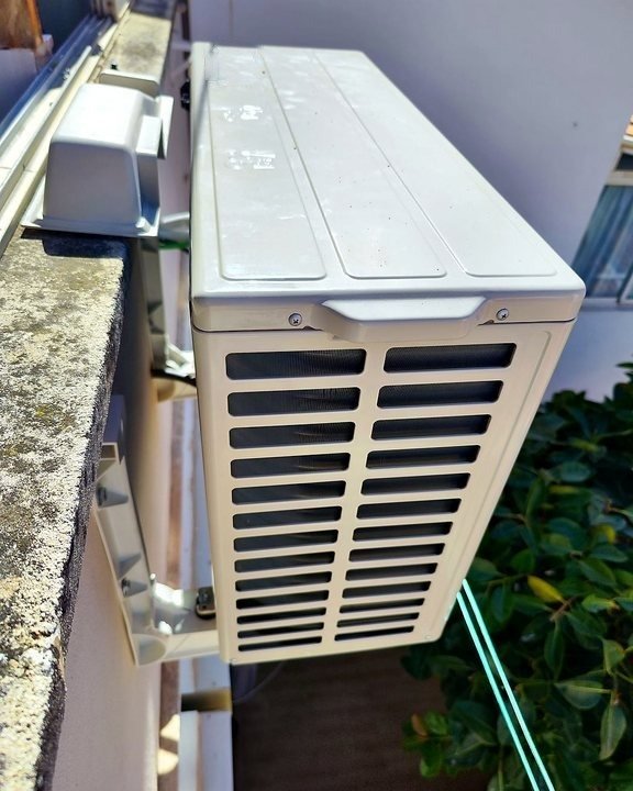 Unidad exterior de aire acondicionado colgada con soportes en un balcón, junto a las plantas, una instalación nuestra en Mallorca