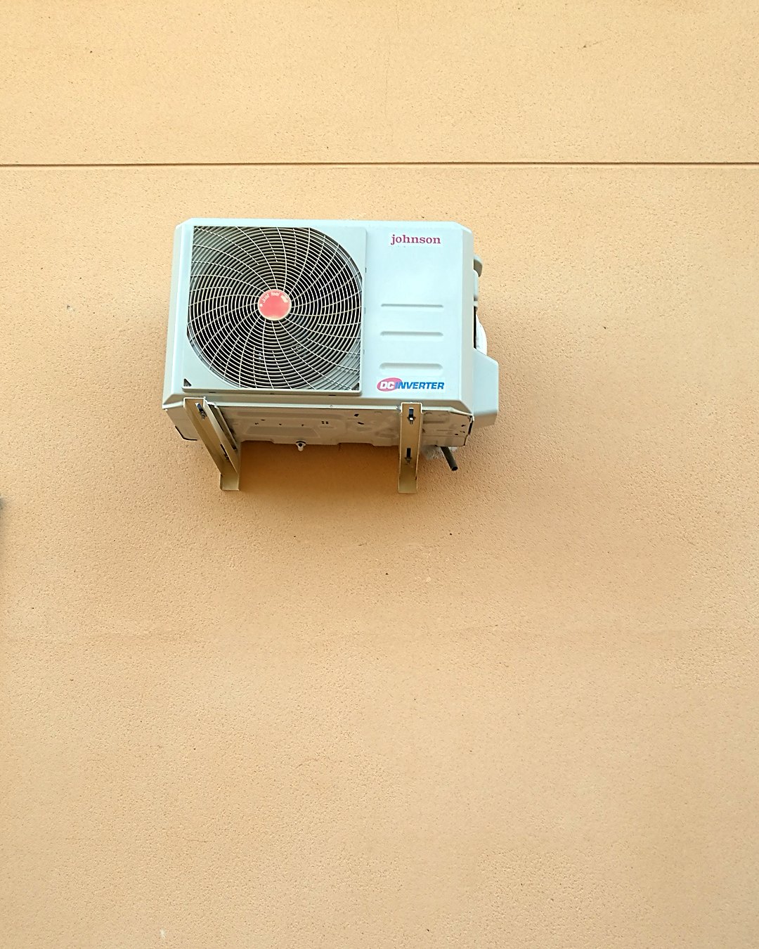 Unidad exterior de aire acondicionado Johnson inverter sobre soportes en una fachada de color arena, en Mallorca