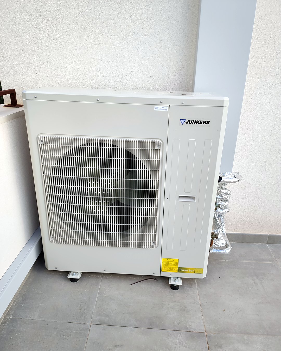 Unidad exterior de bomba de calor Junkers inverter apoyada en una terraza, con las líneas frigoríficas aisladas, en una vivienda de Mallorca