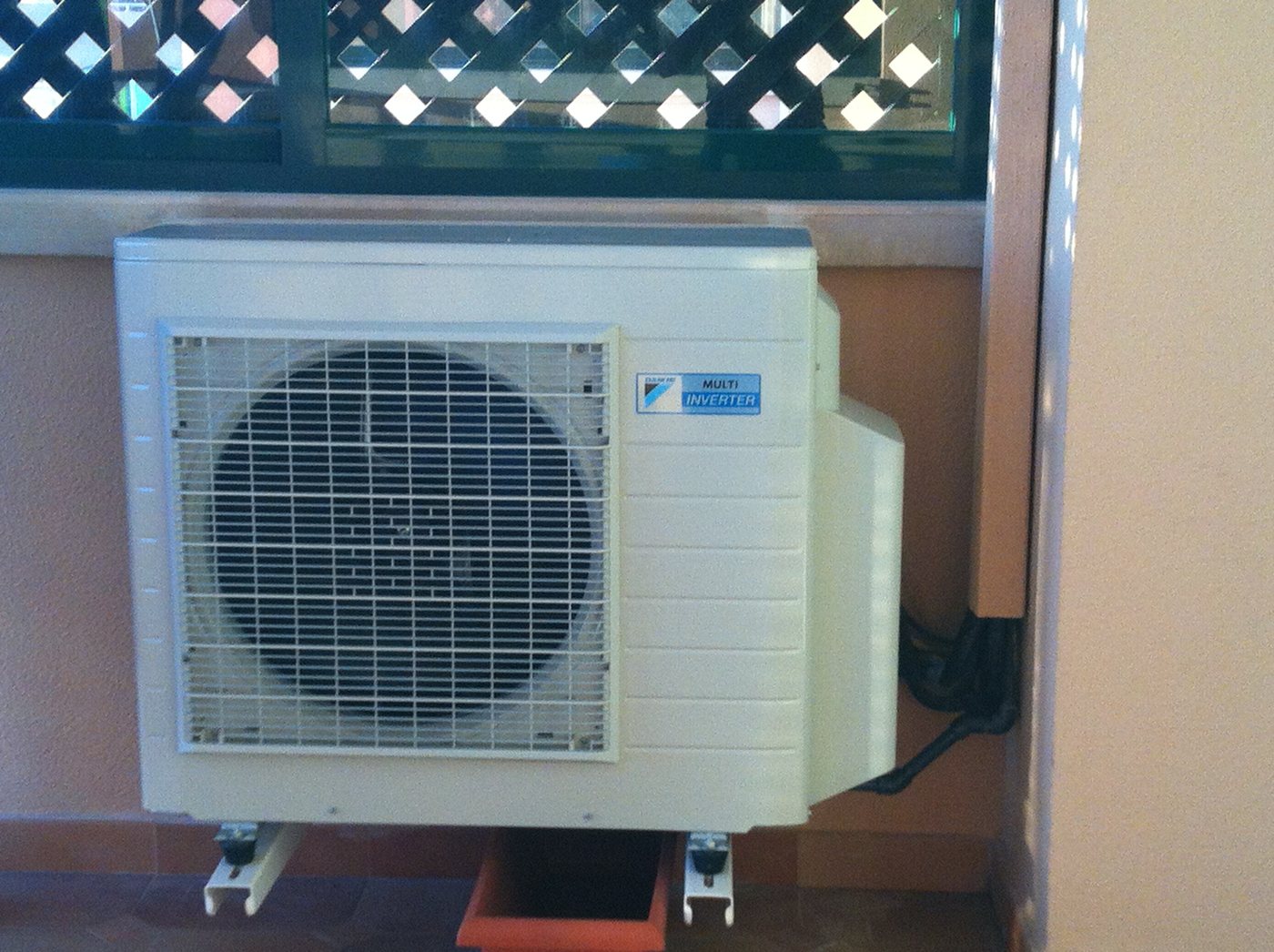 Unidad exterior de aire acondicionado multi inverter colgada con soportes bajo un alero de madera, sobre una celosía, en Palma
