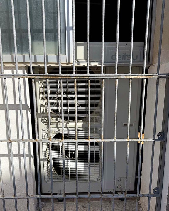 Unidad exterior de aire acondicionado detrás de una reja metálica, bajo una ventana, una instalación nuestra en Mallorca