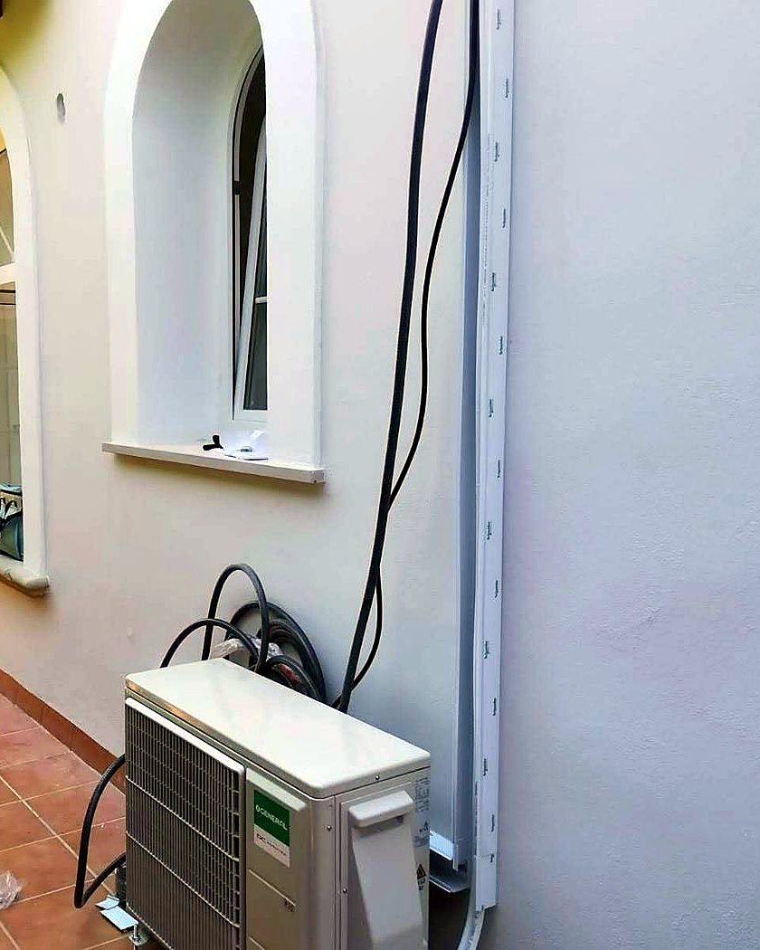 Unidad exterior de aire acondicionado en el suelo de una terraza, junto a una ventana en arco, instalada por JSL en Mallorca
