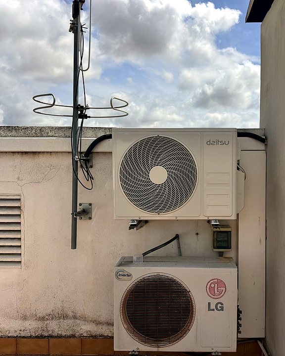 Dos unidades exteriores de aire acondicionado, una sobre otra, en la pared de una azotea bajo un cielo con nubes, una instalación nuestra en Mallorca