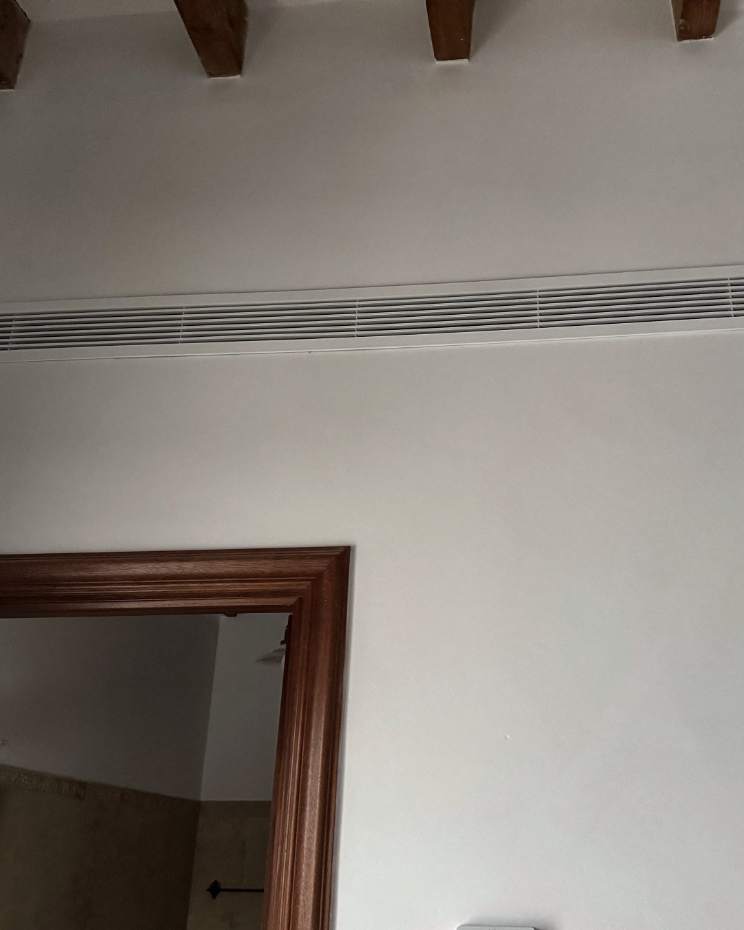 Rejilla lineal de aire acondicionado por conductos integrada bajo vigas de madera, en una vivienda climatizada por JSL en Mallorca