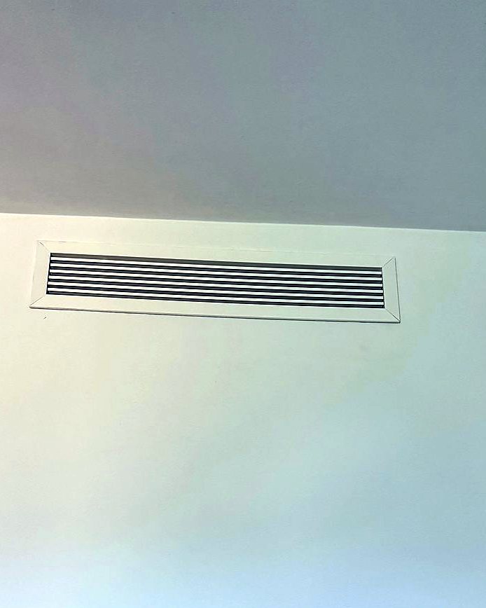 Rejilla de impulsión de aire acondicionado por conductos en lo alto de una pared blanca, montada por JSL en Mallorca
