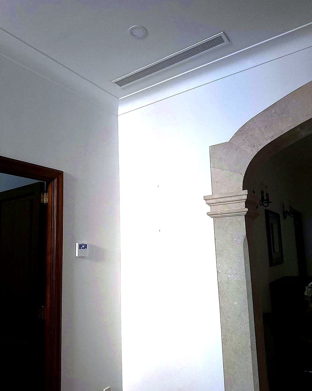 Rejilla lineal de aire acondicionado por conductos en el techo de una casa con arco de piedra y termostato en la pared, montada por JSL en Mallorca