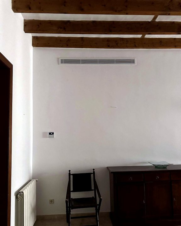 Rejilla lineal de aire acondicionado por conductos bajo un techo de vigas de madera, en una casa de pueblo, una instalación nuestra en Mallorca
