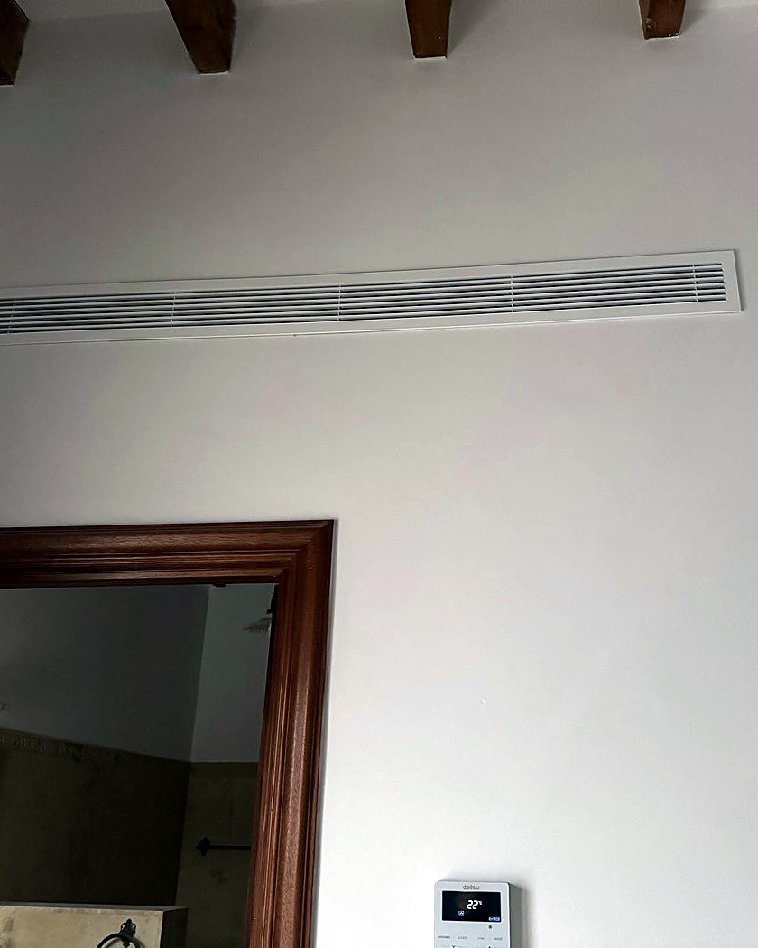 Rejilla lineal de aire acondicionado por conductos bajo las vigas de madera de una habitación, obra de JSL en Mallorca
