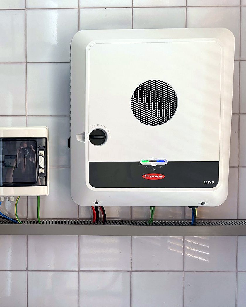 Inversor híbrido Fronius Primo GEN24 con su cuadro de protecciones sobre una bandeja, en una pared alicatada, montado por JSL en Mallorca