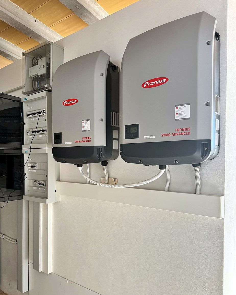 Dos inversores Fronius con sus cuadros de protección en la sala técnica de una instalación fotovoltaica, bajo un techo de vigas, montados por JSL en Mallorca