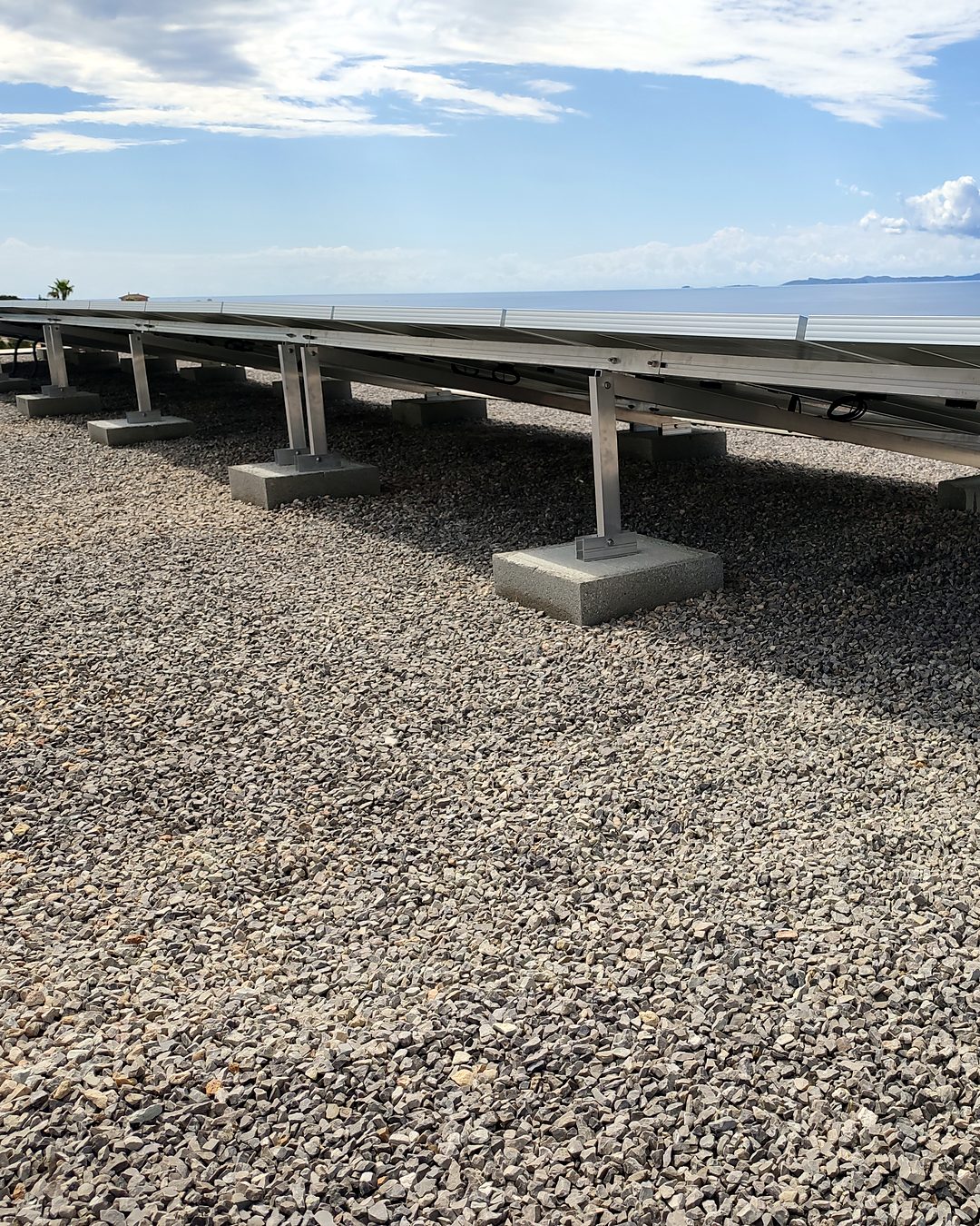 Hilera de placas solares sobre estructura con lastres de hormigón en una azotea de grava con el mar al fondo, instalada por JSL en Mallorca