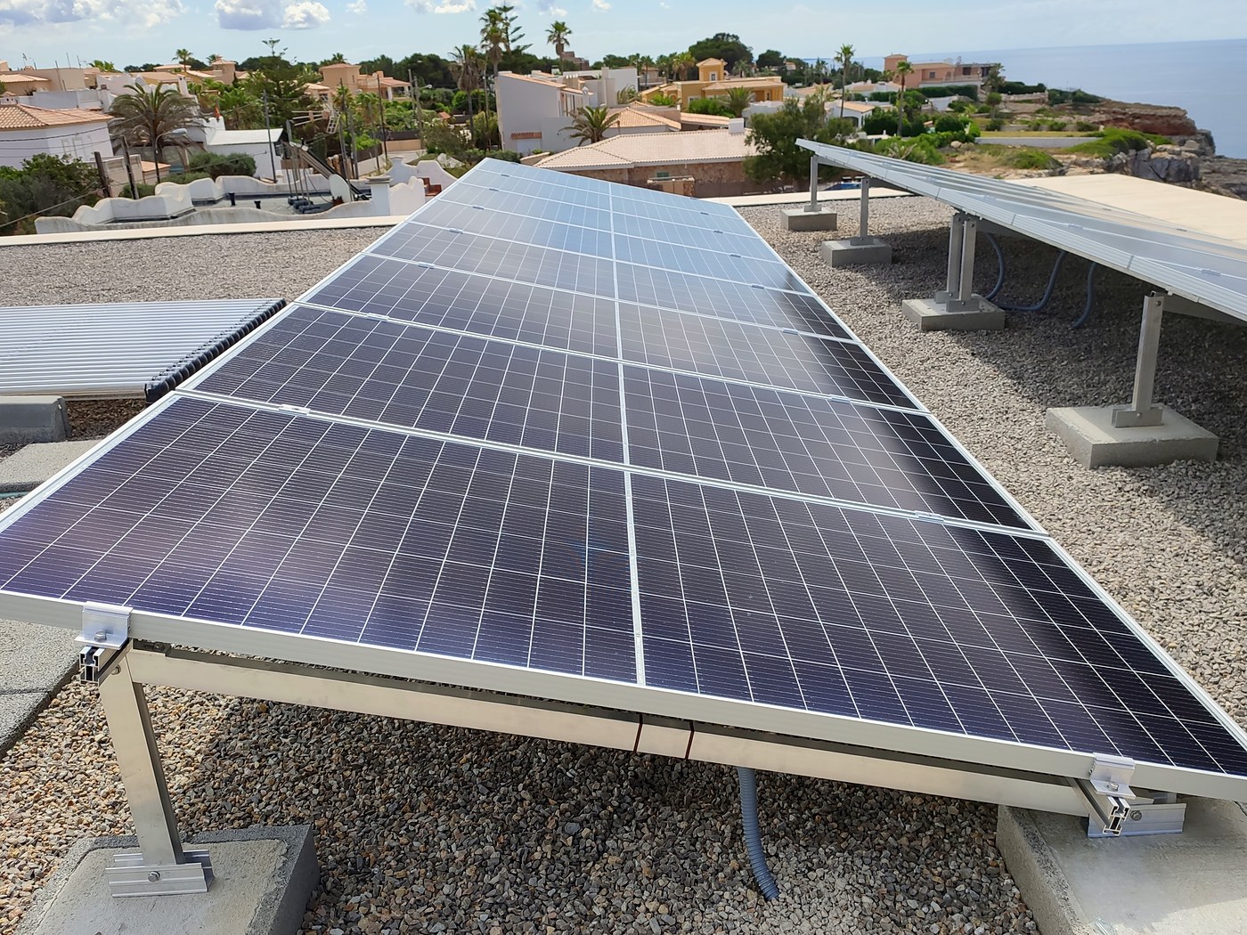 Placas solares sobre estructura en una azotea de grava con el mar al fondo, una instalación nuestra en Mallorca