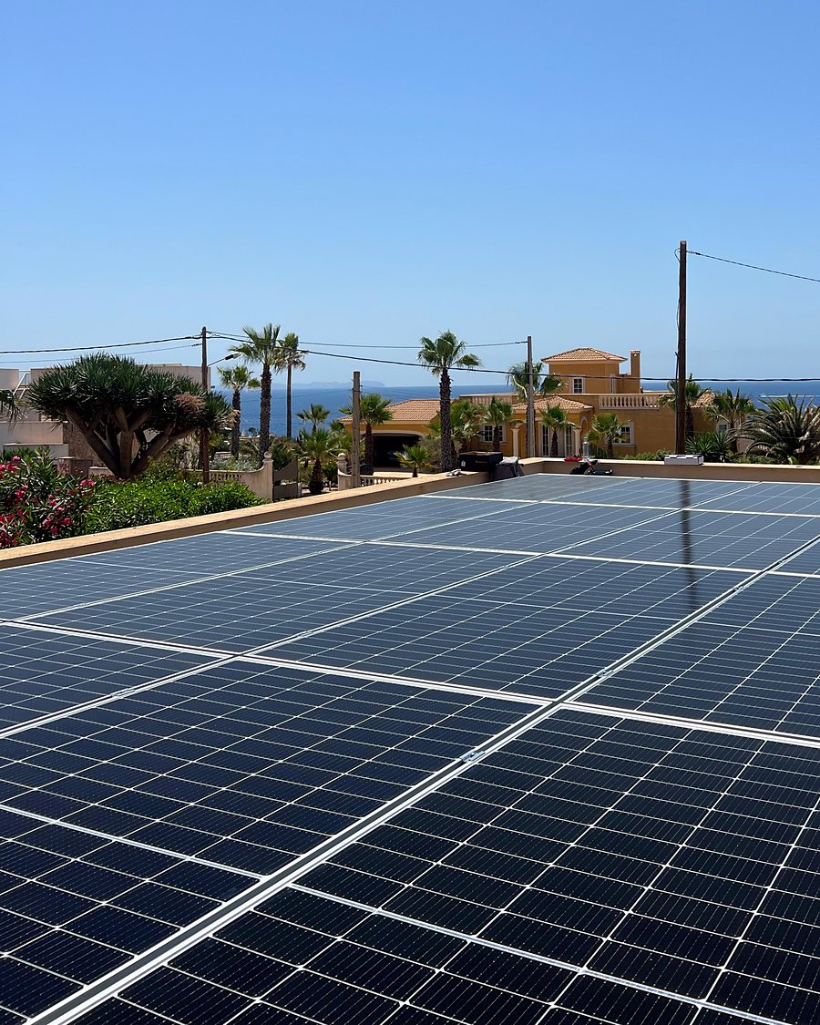Placas solares sobre la azotea plana de una casa de la costa de Mallorca, con palmeras y el mar al fondo, instaladas por JSL