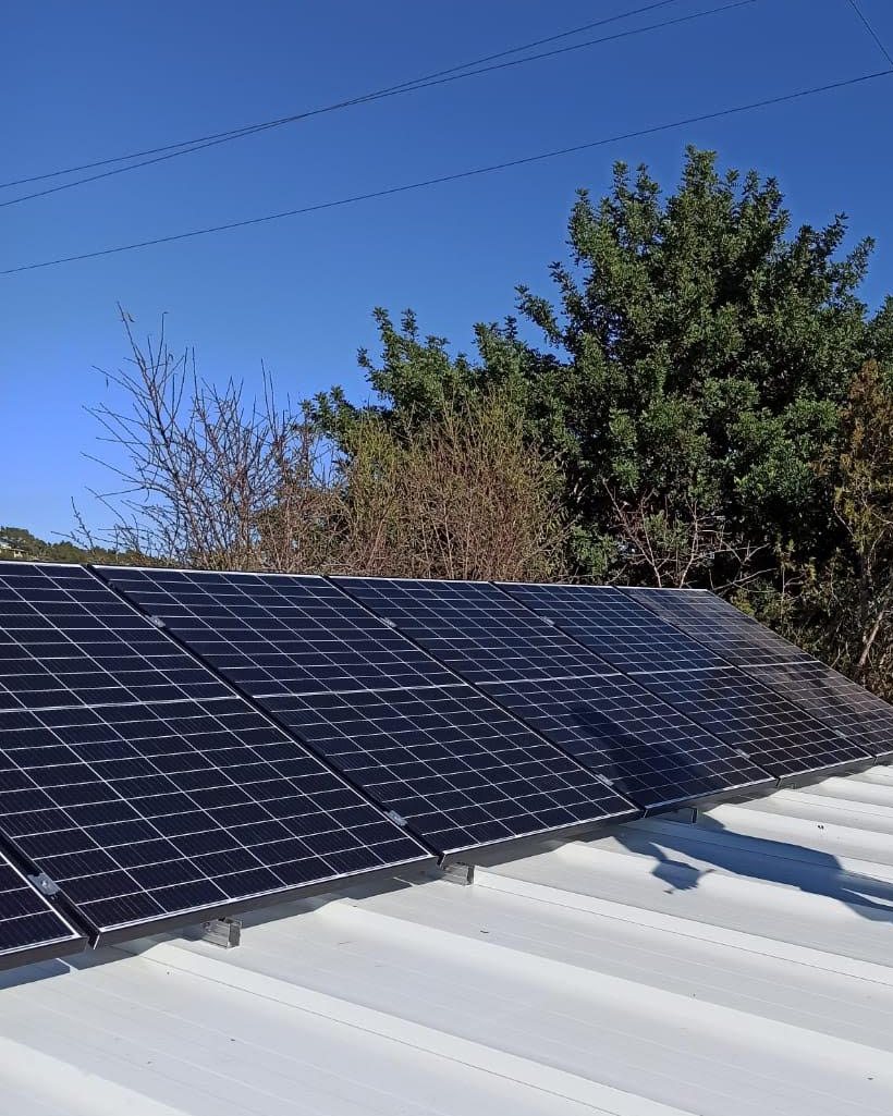 Placas solares sobre estructura inclinada en una cubierta de chapa, con arbolado detrás, instaladas por JSL en Mallorca