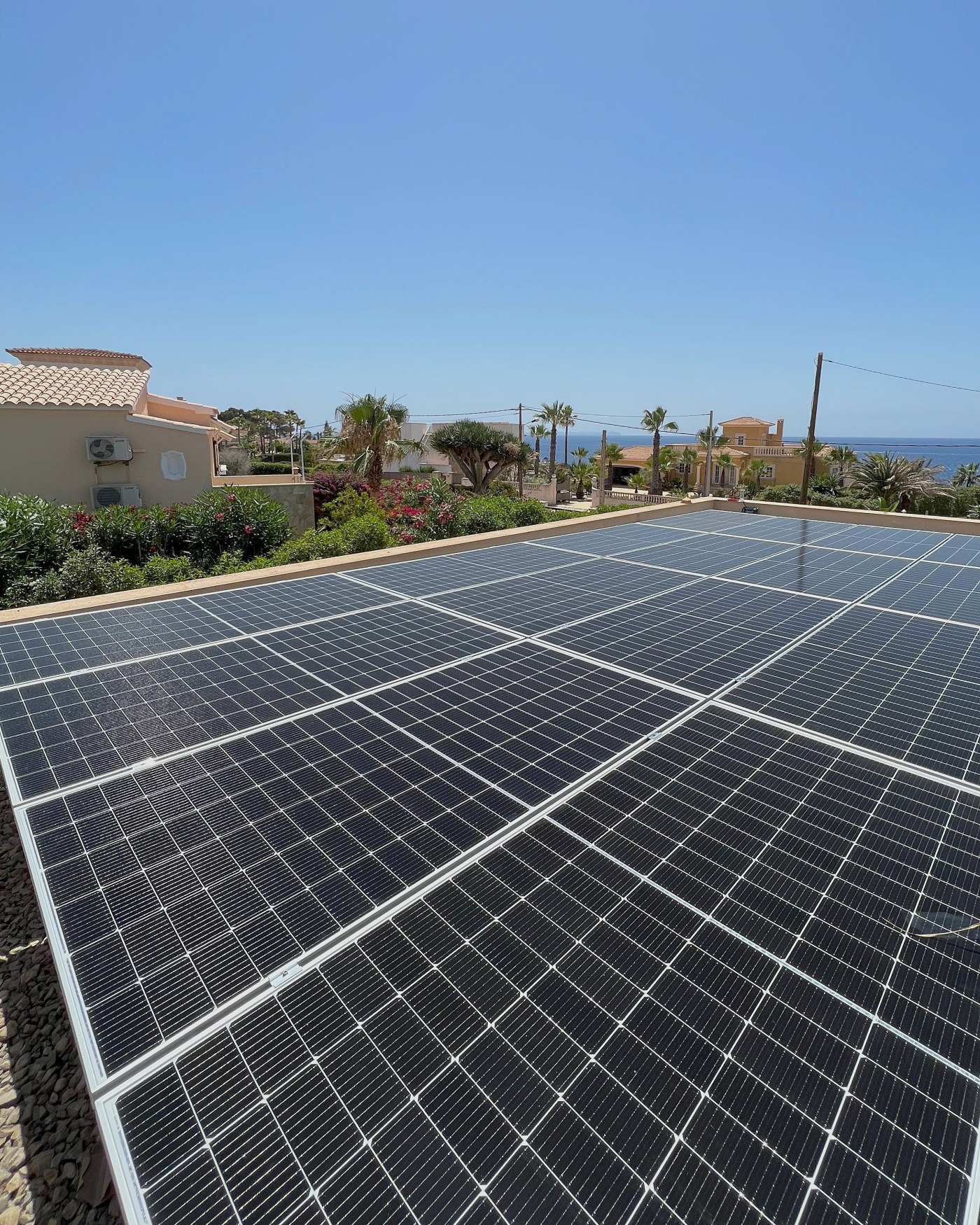 Campo de placas solares sobre una cubierta plana en una instalación de JSL en Mallorca, con el mar al fondo