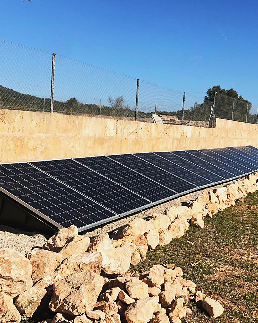 Fila de placas solares en suelo junto a un muro de piedra seca, instalación de JSL en Mallorca