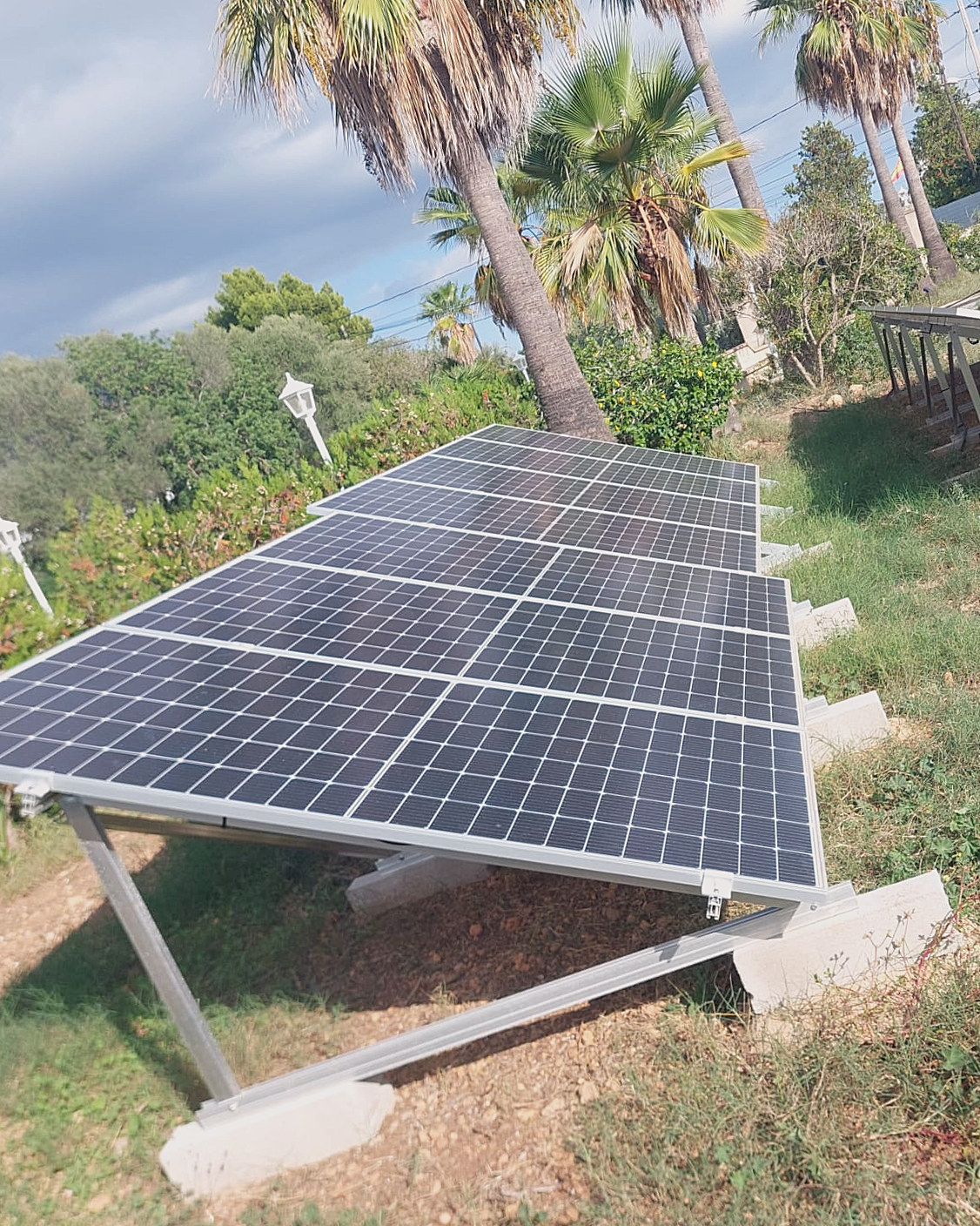 Ground-mounted solar panels in a garden with palm trees, a JSL installation in Mallorca