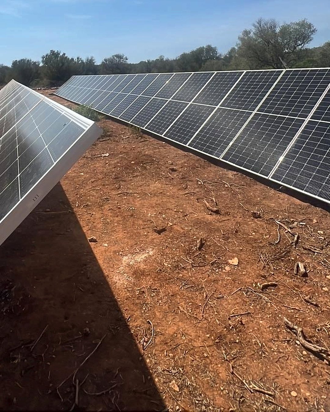 Filas de placas solares sobre estructura en el suelo de una finca de Mallorca, con tierra roja y encinas