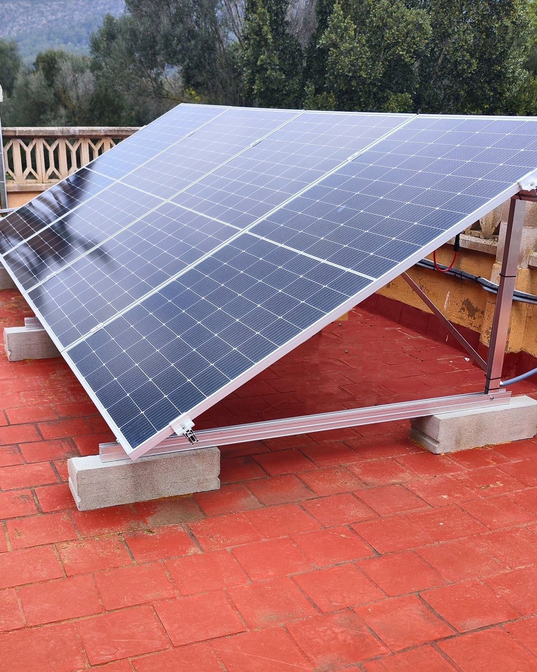Placas solares sobre estructura inclinada en una terraza de baldosa roja, con la sierra al fondo, instalación de JSL en Mallorca
