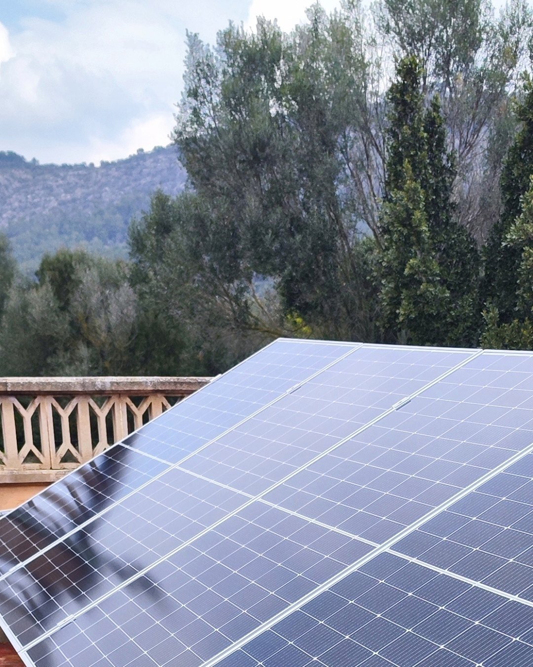 Placas solares sobre estructura inclinada en una terraza de baldosa roja, con la sierra al fondo, instaladas por JSL en Mallorca