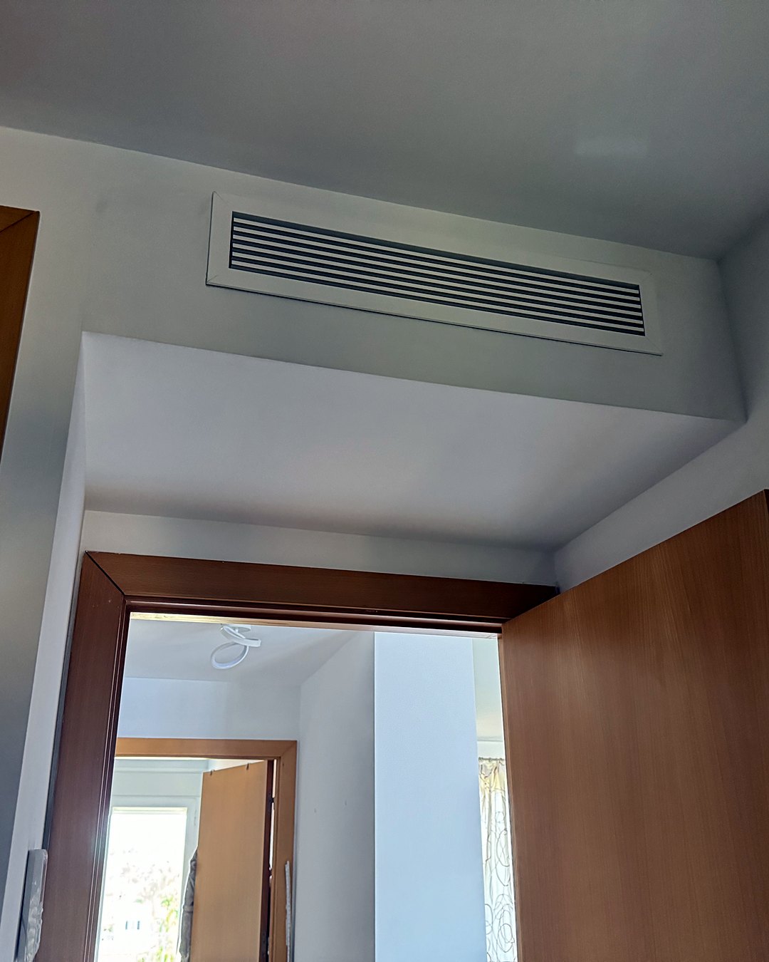 Rejilla de lamas de un aire acondicionado por conductos, en el cajeado del techo sobre una puerta de madera, en una vivienda de Mallorca