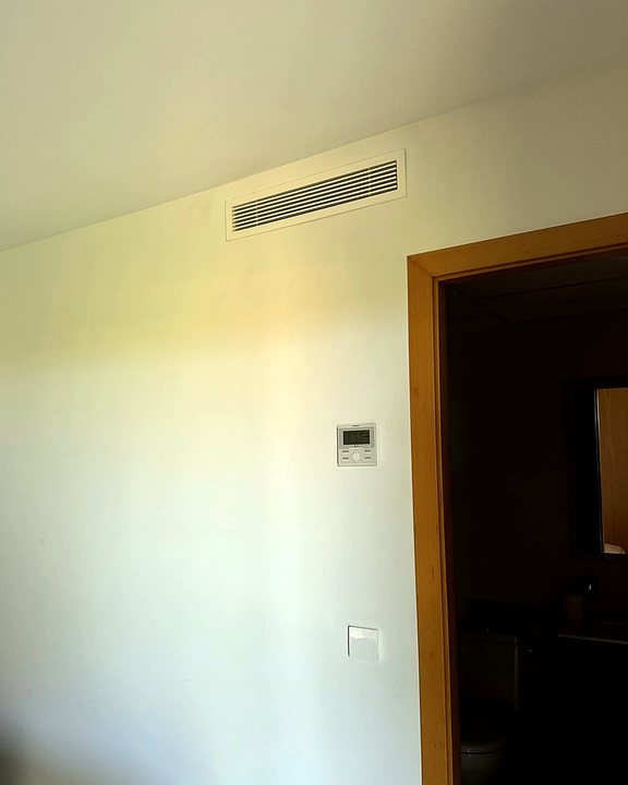 Rejilla lineal de aire por conductos junto al techo y termostato en la pared de un dormitorio, una instalación nuestra en Mallorca