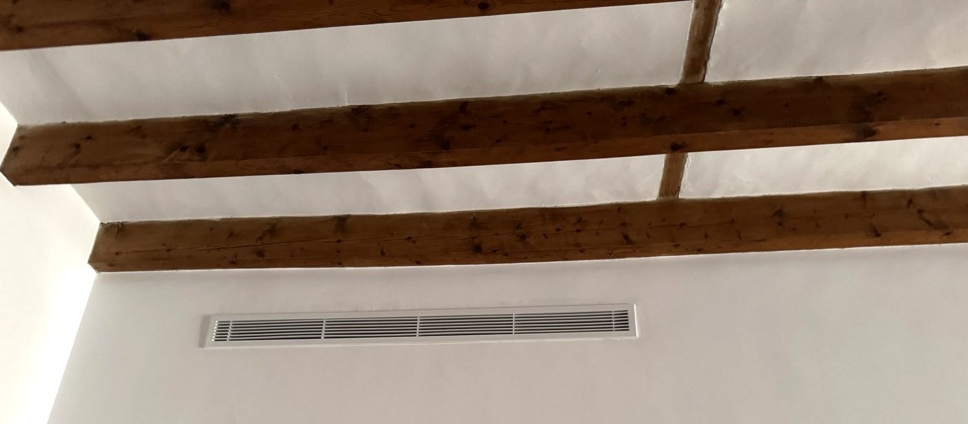 Rejilla lineal de climatización por conductos bajo vigas de madera en una casa de Mallorca