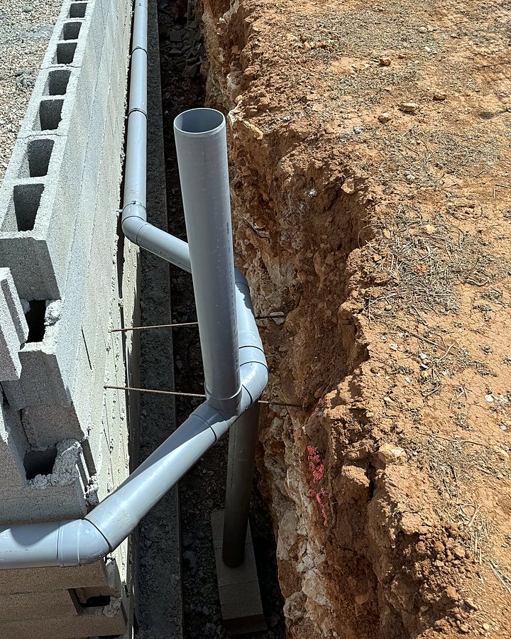 Bajante de PVC con sus codos entrando en la zanja junto al muro, antes de rellenar, en una obra de JSL en Mallorca
