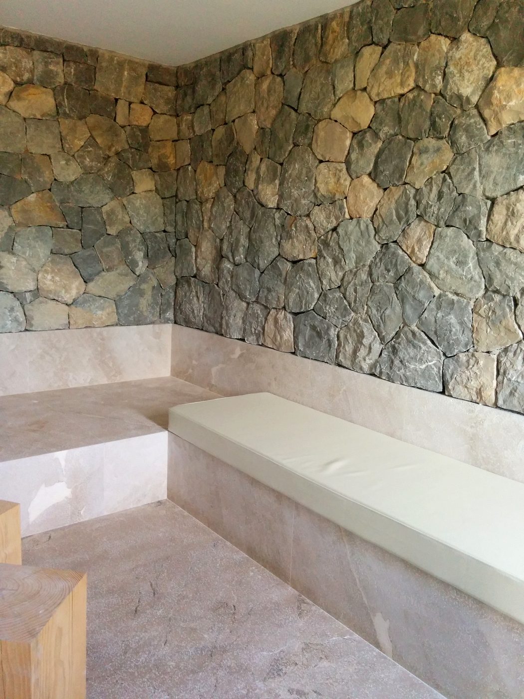 Zona de spa con banco de travertino y pared de piedra natural en la Villa de Port d'Andratx, JSL Mallorca