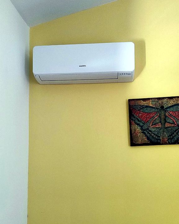 Split de pared blanco instalado en lo alto de una pared amarilla de un dormitorio, una instalación nuestra en Mallorca
