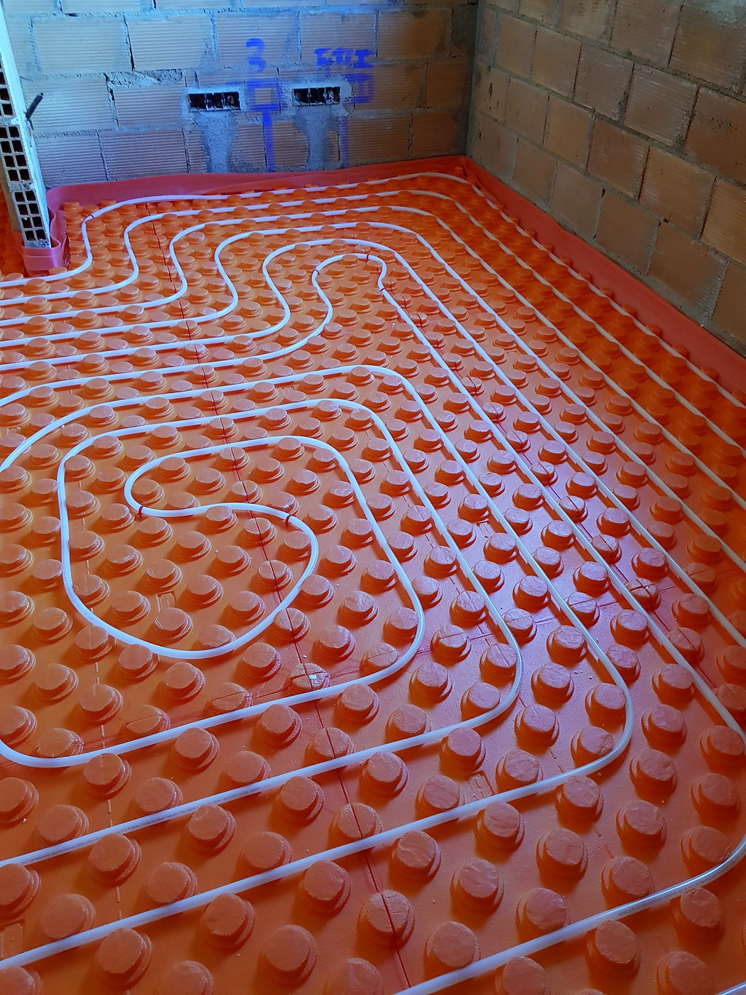 Circuitos de suelo radiante en espiral sobre placa de tetones en una estancia, en una obra nuestra en Mallorca